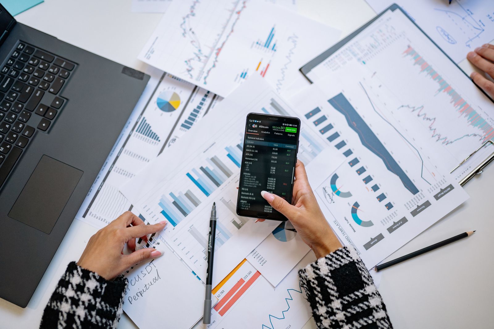 A person reviewing financial charts and market data on a phone and laptop